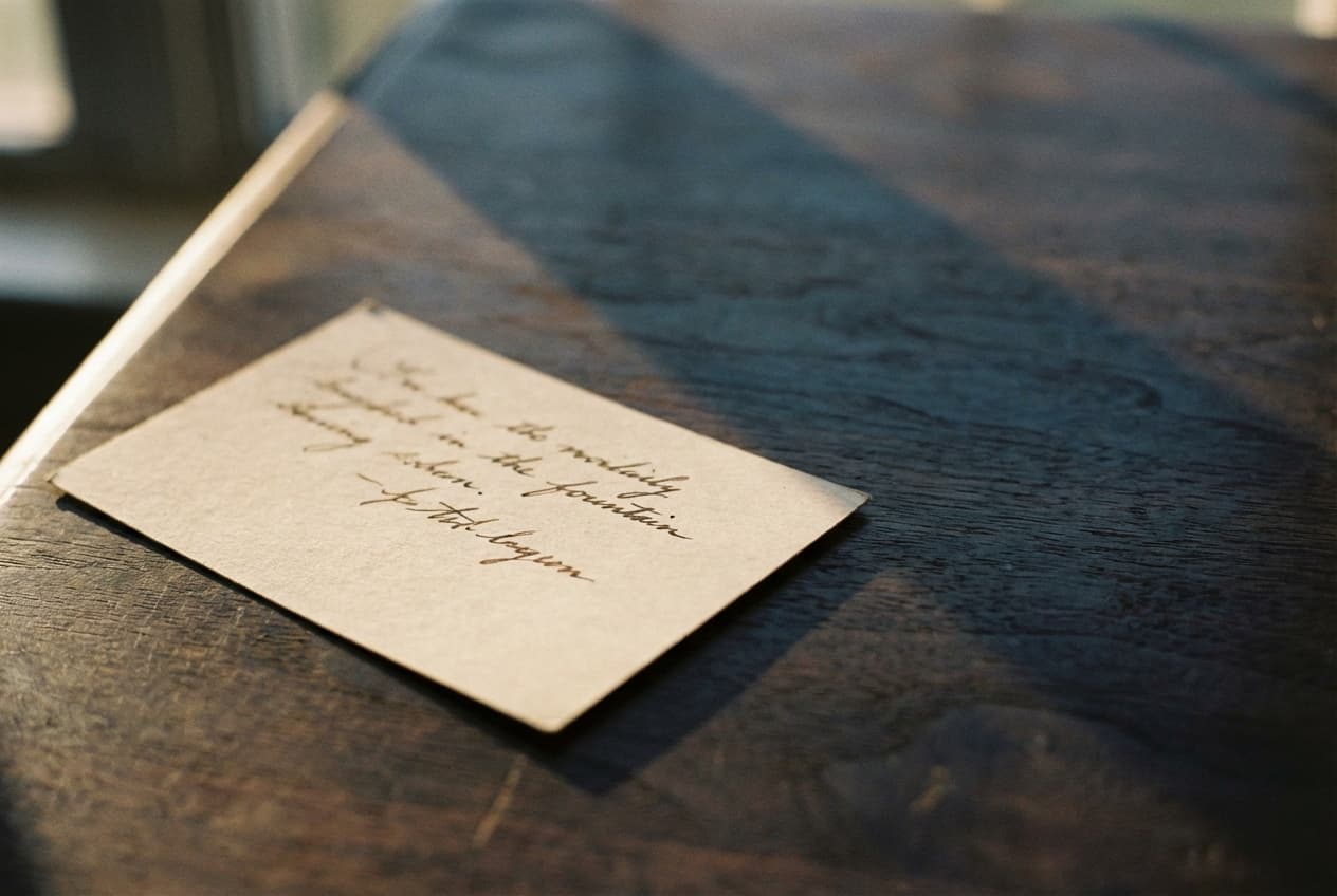 A single cream index card with a few handwritten lines, resting on a dark walnut desk.